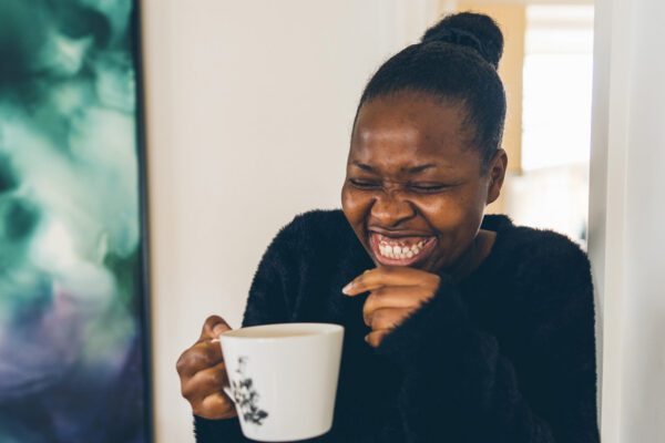 Woman laughing while holding a mug of tea at home