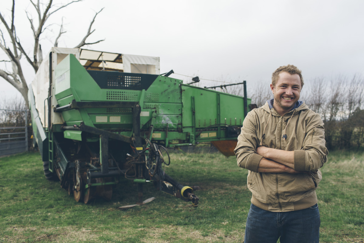 Farm worker standing beside a potato harvester, smiling with arms crossed